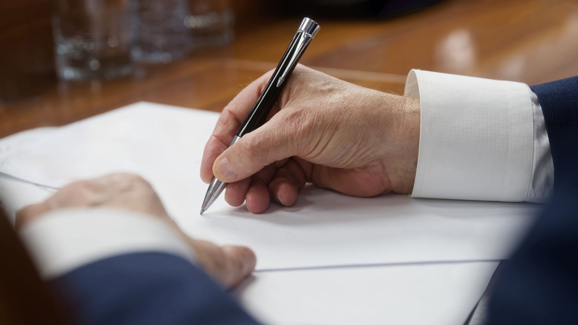 Hand holding pen signing legal document on wooden desk during official paperwork process.