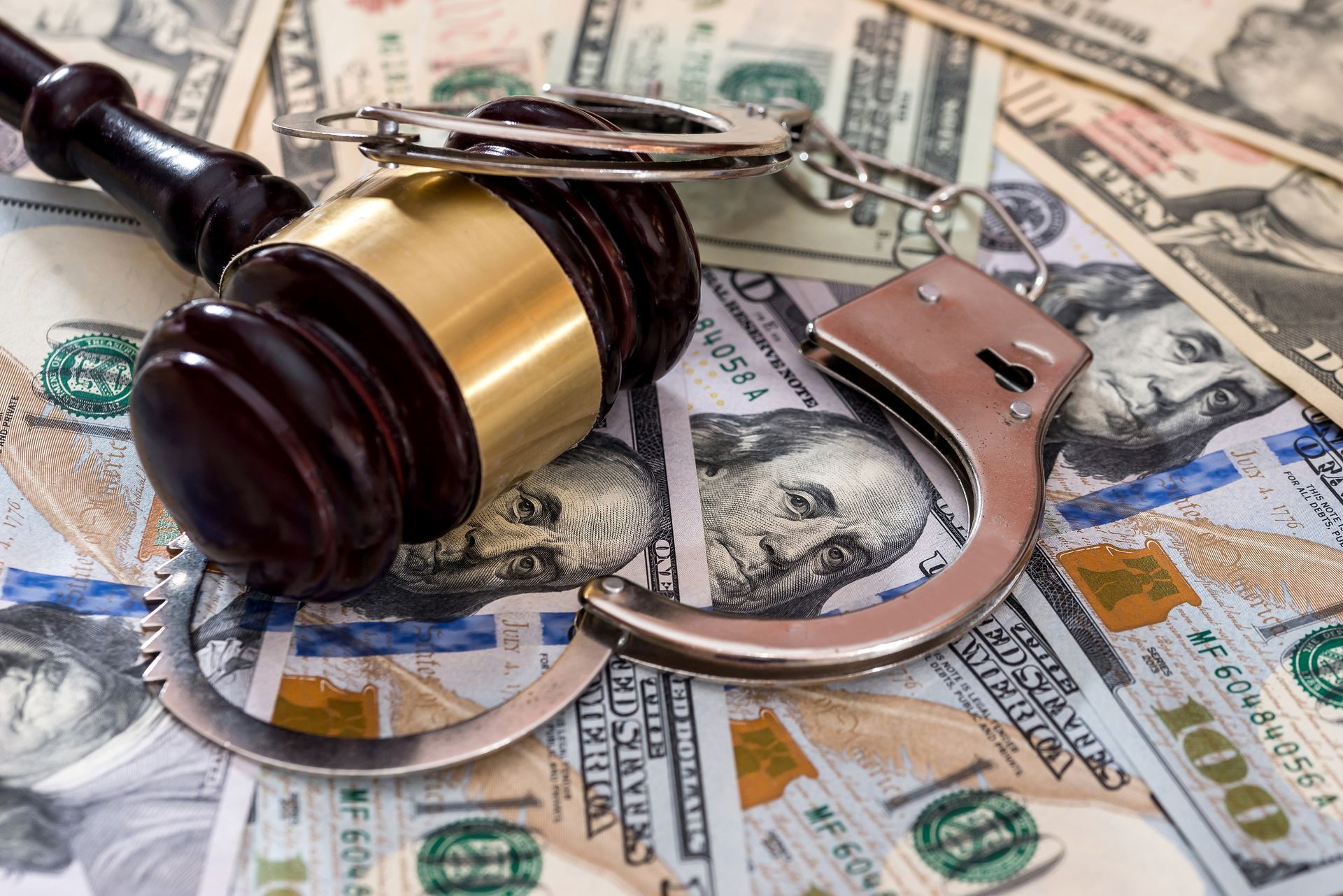 Gavel and handcuffs on a bed of US dollar bills, symbolizing financial crime or legal action.