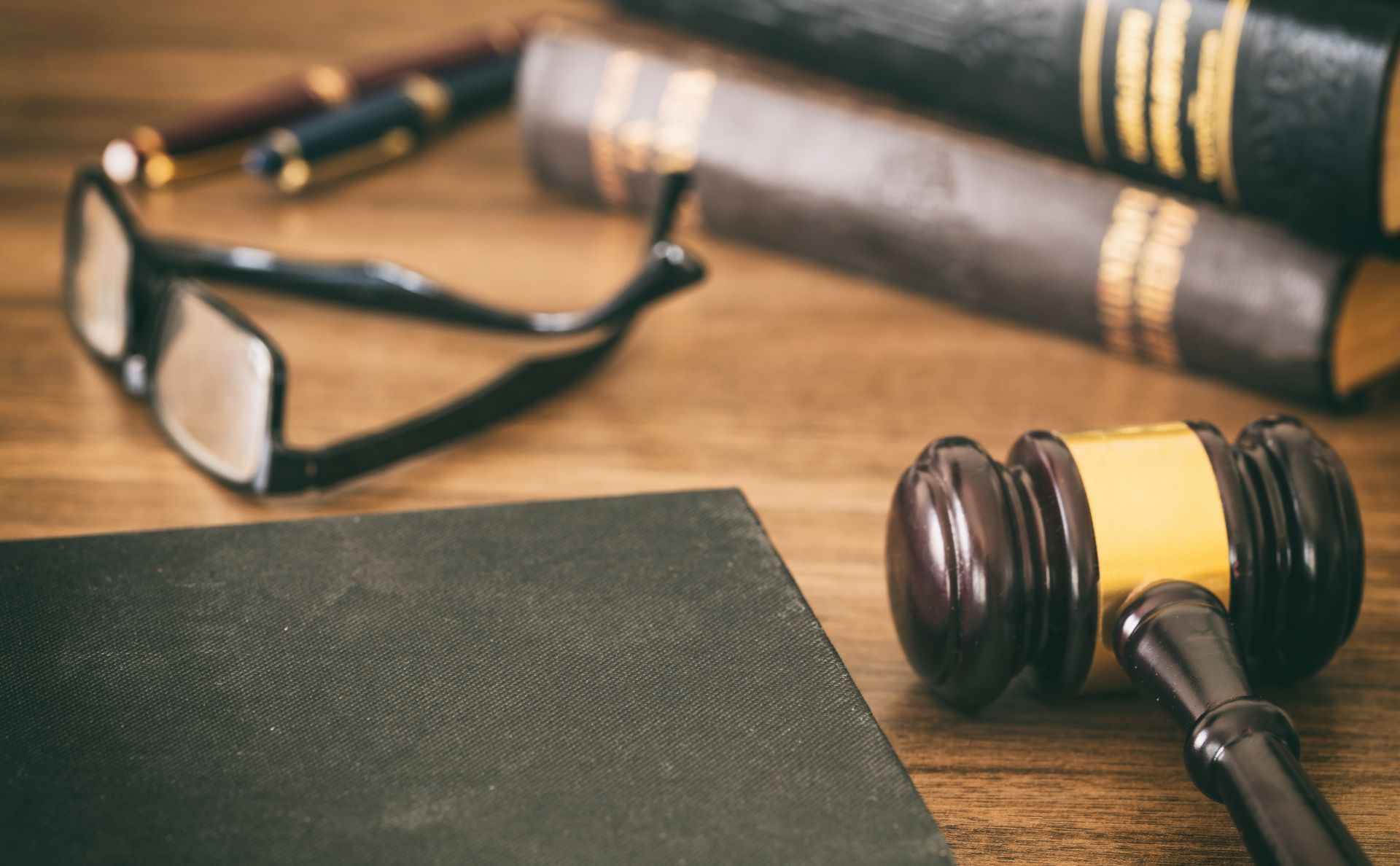 Gavel, books, glasses, and pens on a wooden desk, suggesting a legal or academic setting.