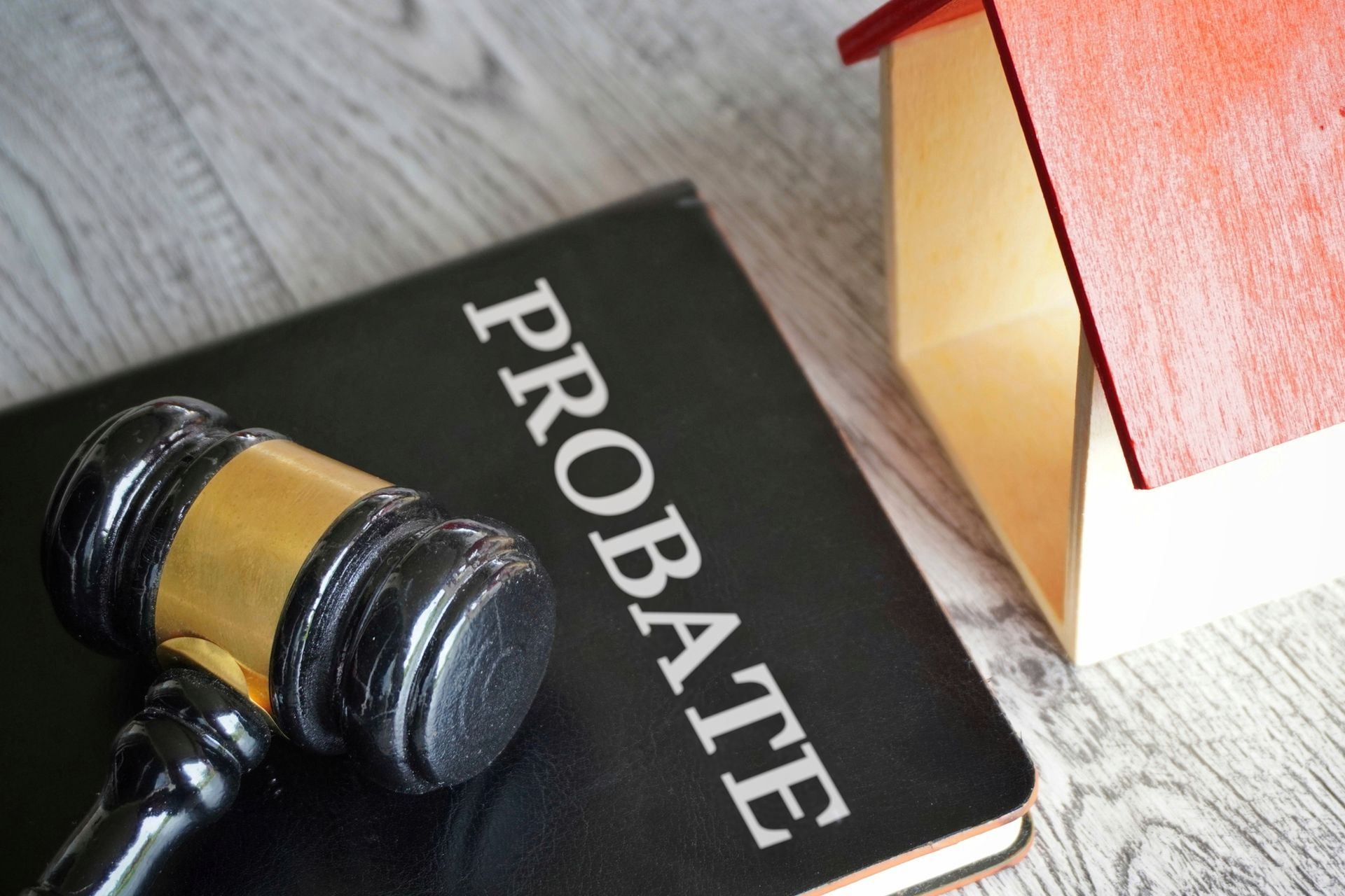 Toy house with red roofing, gavel and text PROBATE displayed on a black book.