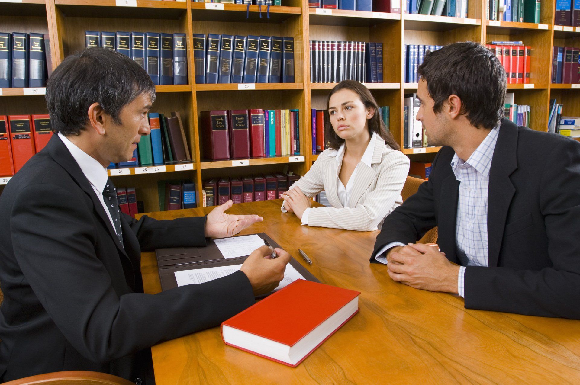 Lawyer speaking to a couple at a table in a library, discussing documents.