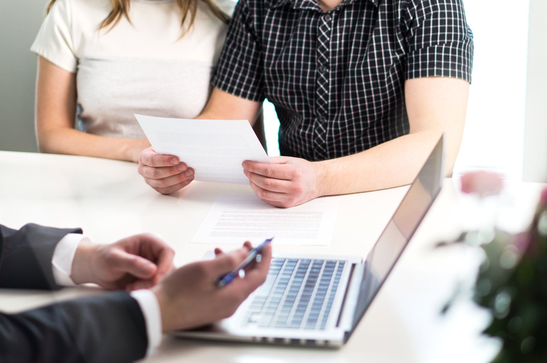 Couple reviewing documents with a financial advisor; laptop and pen visible.