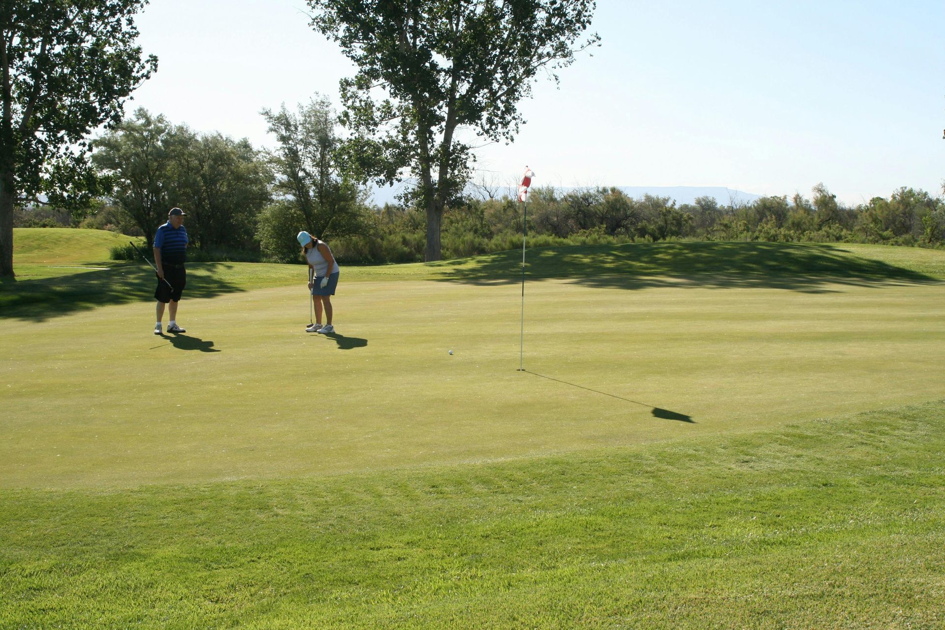 Two golfers on a green putting surface near the hole, with trees and fairway in the background