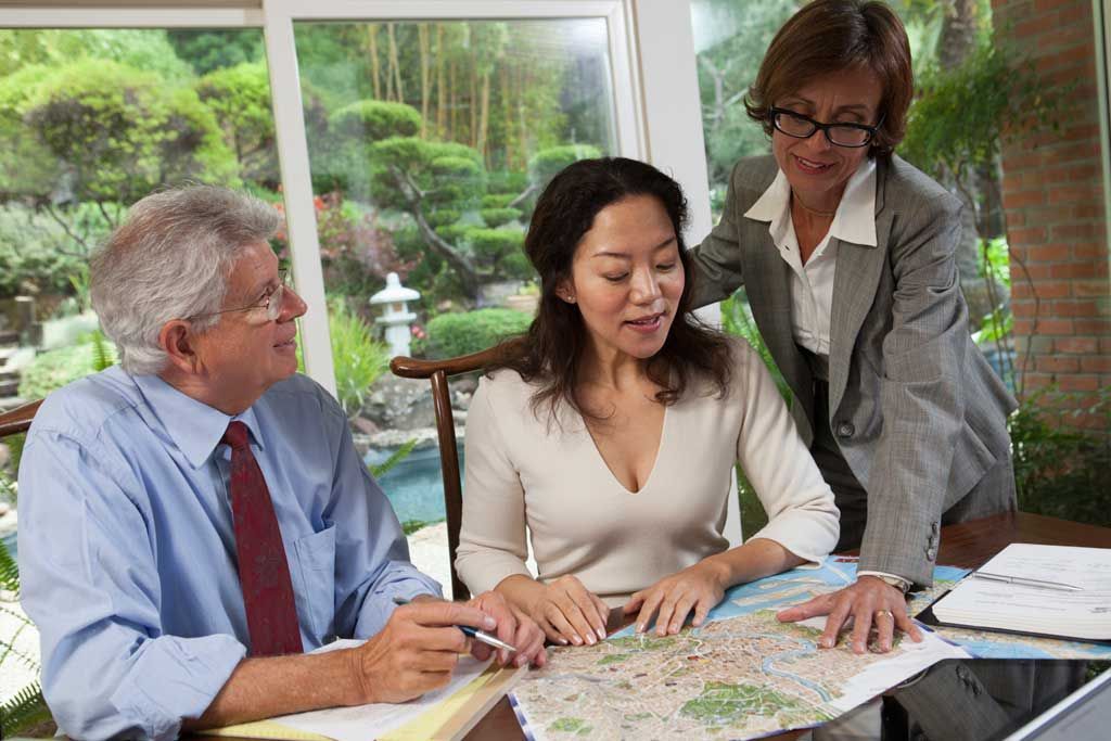 Three colleagues review a map and documents at a table in a bright office.