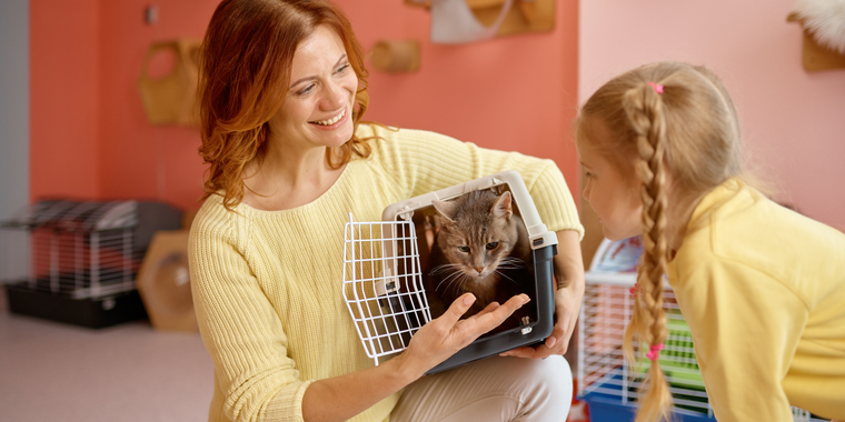 A woman is holding a cat in a cage while a little girl looks on.