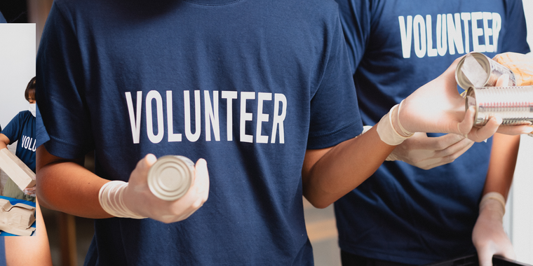 Two volunteers are holding cans of food in their hands.