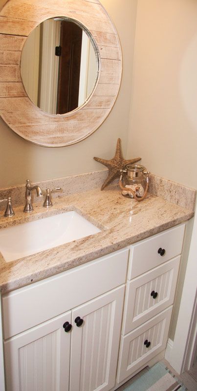 Bathroom vanity with a round mirror, seashell decor, and white cabinets.