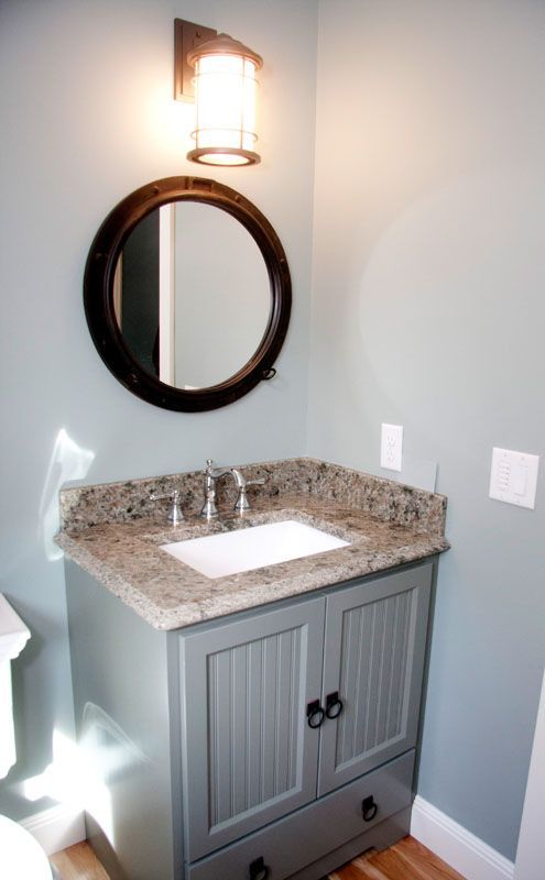 Bathroom with gray vanity, round mirror, granite countertop, and sconce.