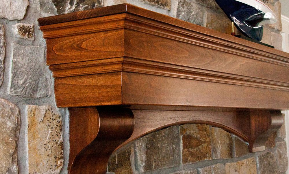 Wooden fireplace mantel with ornate carvings against a stone wall.