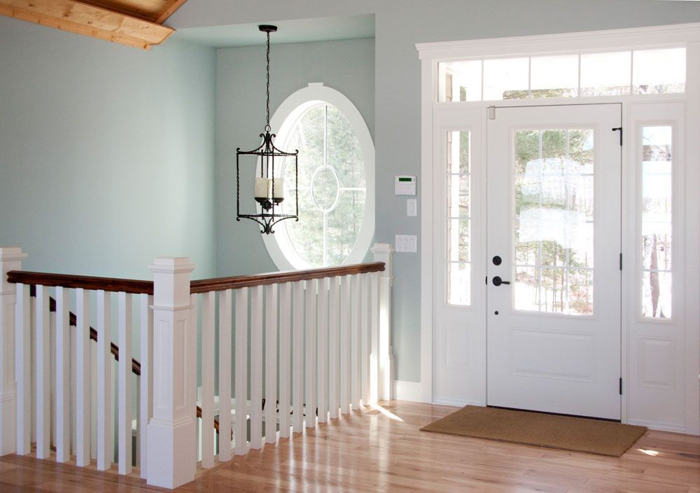 Light blue walls and white trim frame a staircase and front door with a decorative window.
