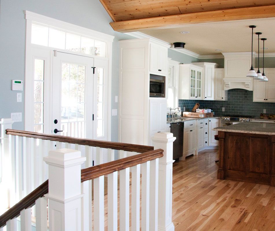 Bright kitchen with white cabinets, wood island, and light blue walls, visible from the top of a wooden staircase.