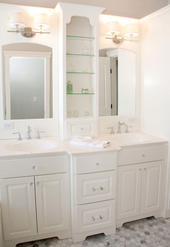White bathroom vanity with two sinks, mirrors, glass shelves, and cabinets.