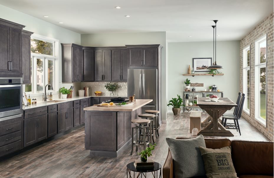 Kitchen with gray cabinets, stainless steel appliances, island, and dining area with exposed brick wall.