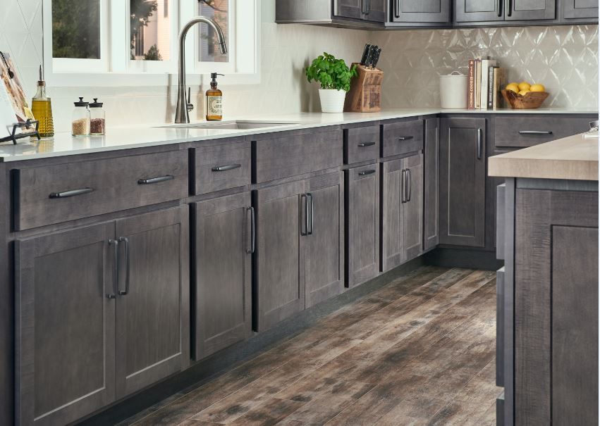 Gray kitchen cabinets with black handles, a white countertop, and wood-look flooring.