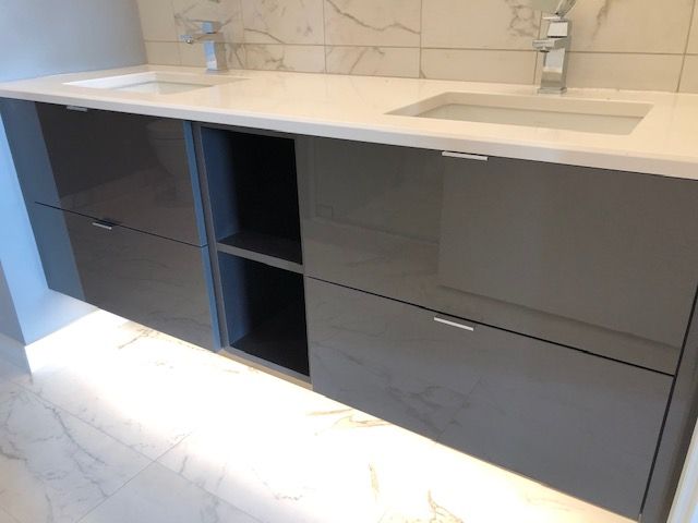 Gray vanity with a white countertop and two sinks. Open shelf in the center.