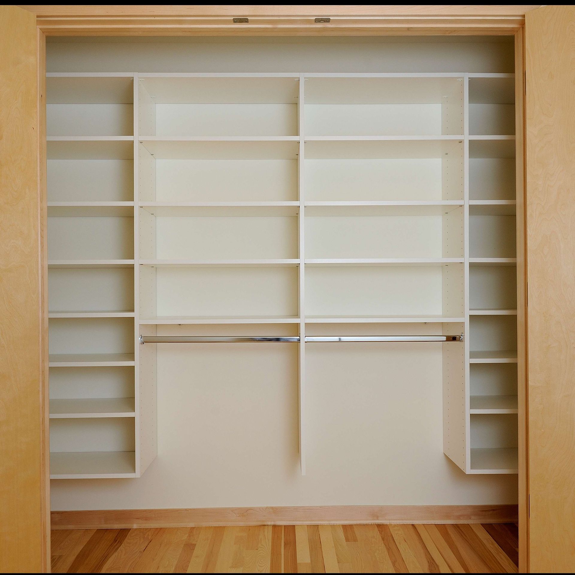 Empty white closet with shelves and hanging rods, built into a wall.