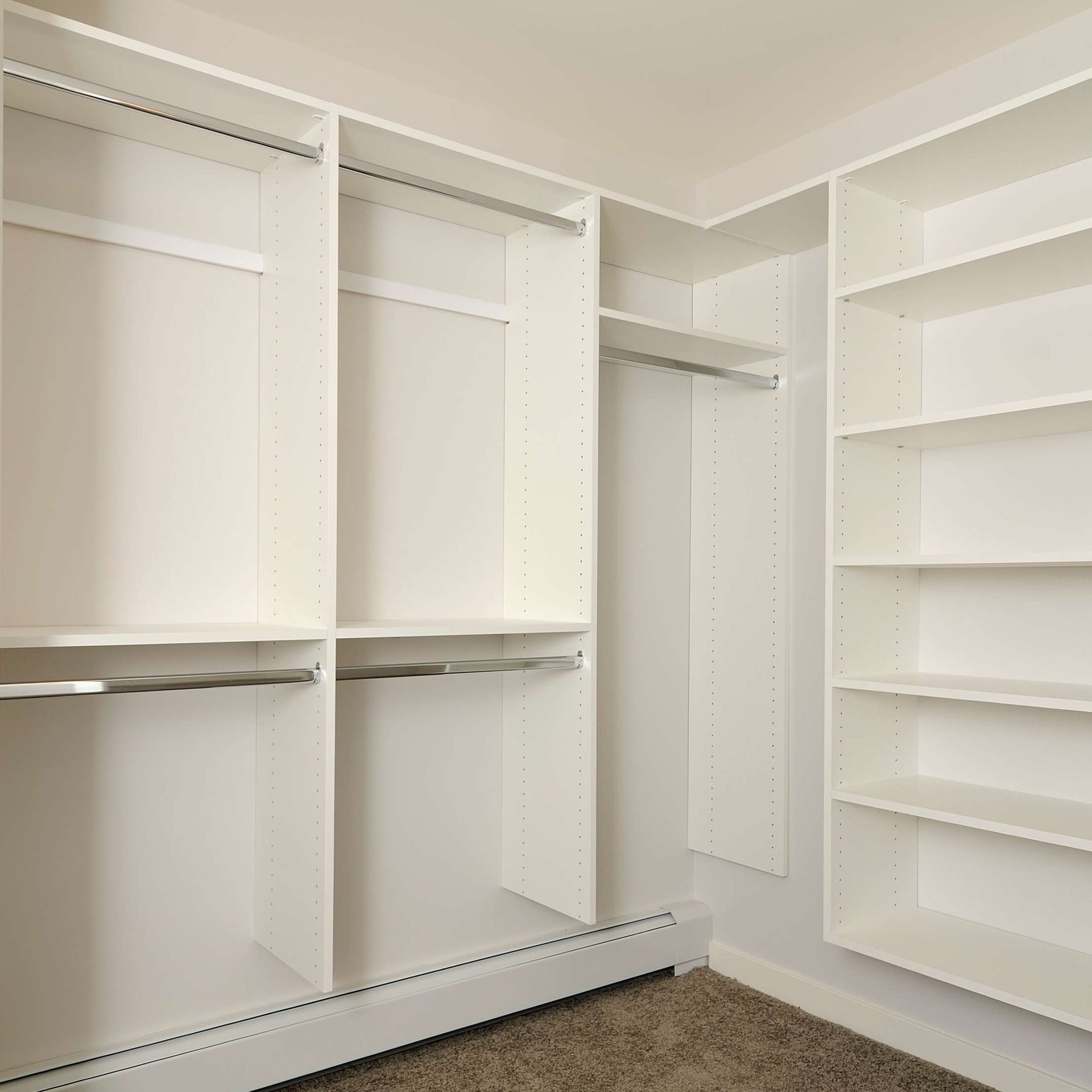 Empty white closet shelving with hanging rods and shelves, built-in on carpet.