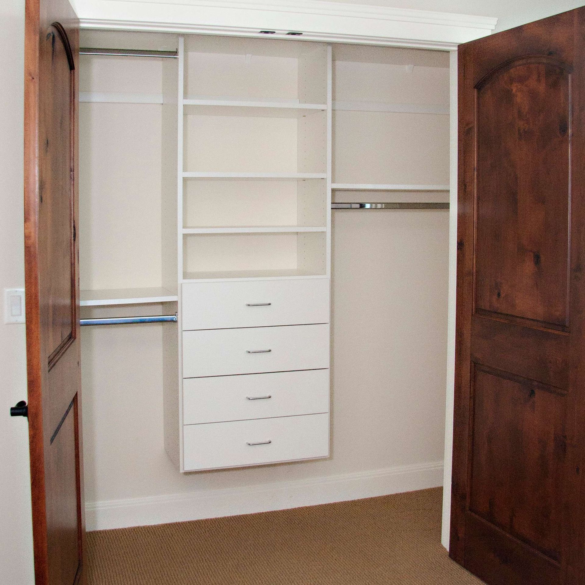Closet interior with white shelving, drawers, and hanging rods. Two wooden doors.