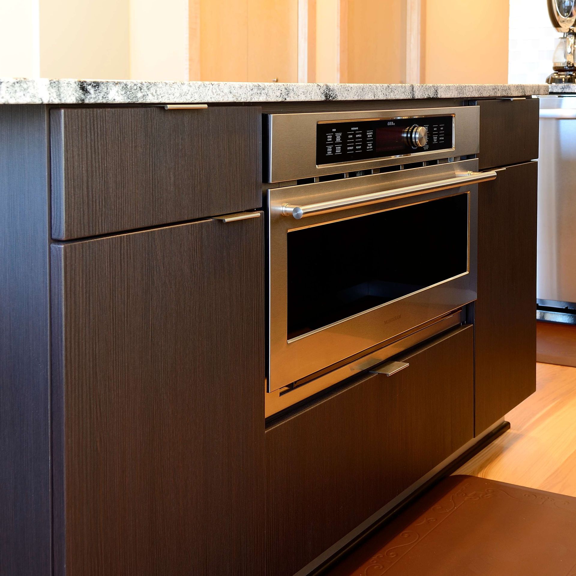 Built-in stainless steel microwave oven in a dark wood cabinet island, granite countertop.