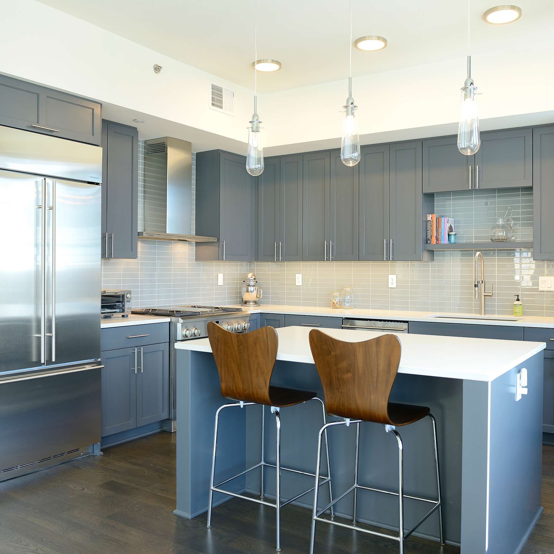 Modern kitchen with gray cabinets, stainless steel appliances, and a white countertop island with two bar stools.