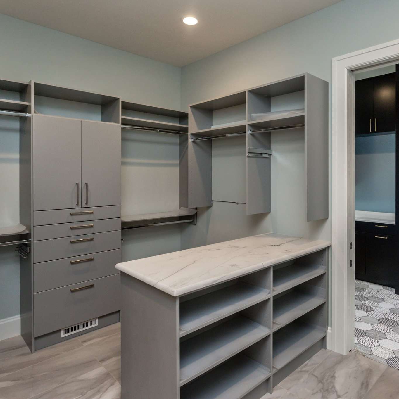 Gray walk-in closet with shelves, hanging rods, and a center island. Light blue walls, gray flooring.