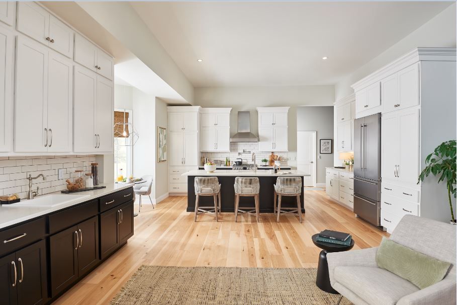Spacious white kitchen with dark island and cabinets, hardwood floors, and stainless steel appliances.