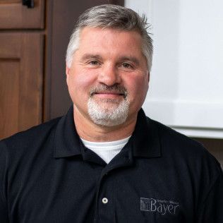 Man with graying hair and beard in a black polo shirt, smiling at the camera.