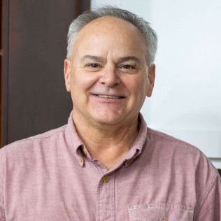 Smiling man with graying hair wearing a pink button-down shirt.