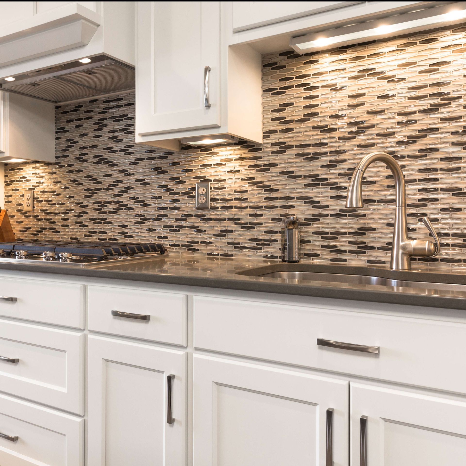 White kitchen cabinets with dark countertop, stainless steel sink, and mosaic backsplash.