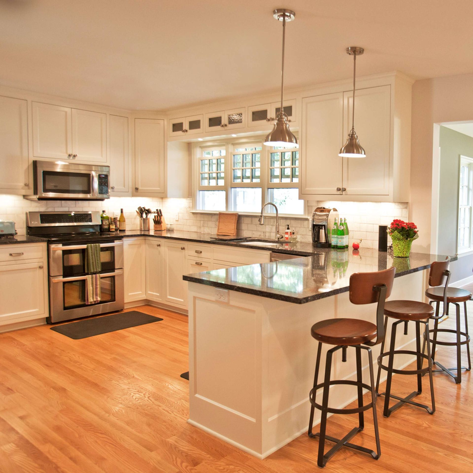 Bright kitchen with white cabinets, stainless steel appliances, and a granite island with stools.