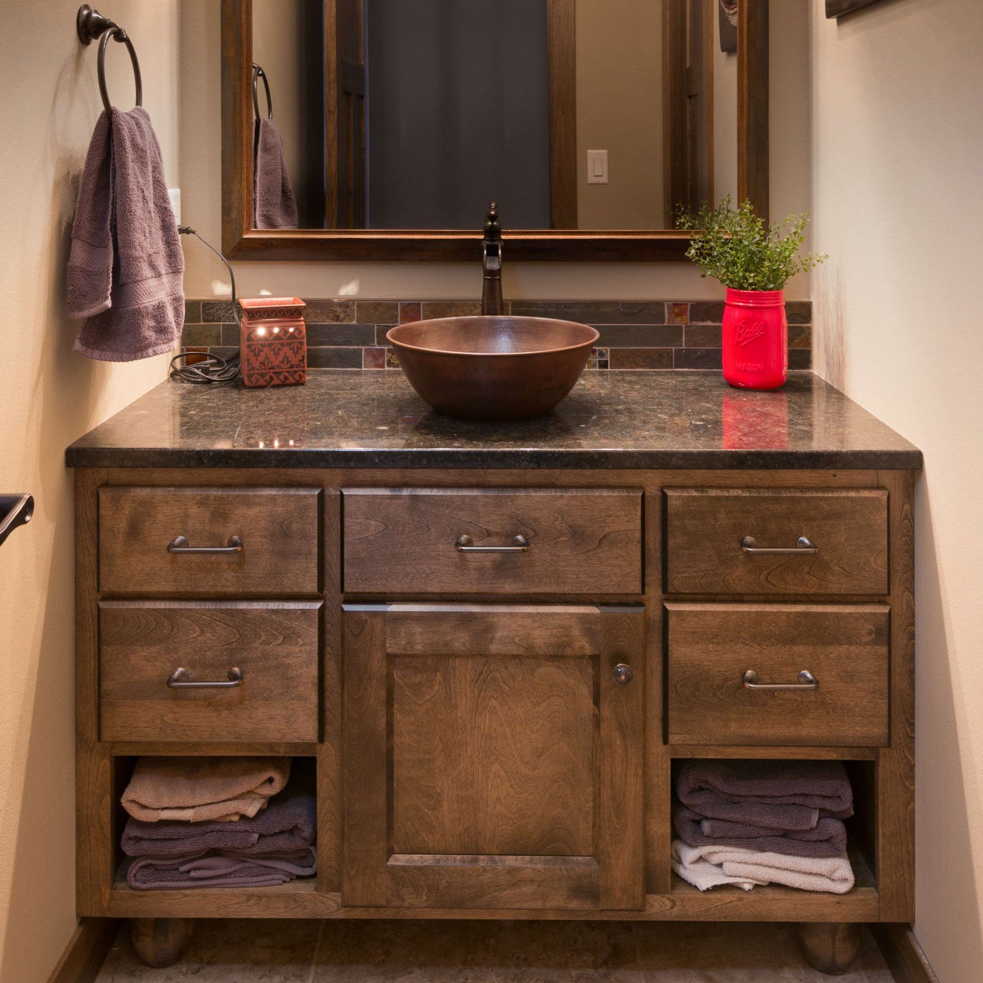 Bathroom vanity with wooden cabinet, copper sink, and decorative elements.