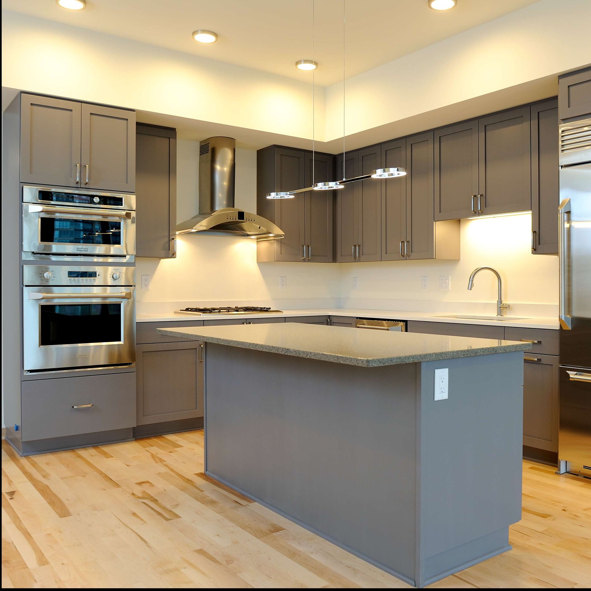 Modern gray kitchen with stainless steel appliances, island, and wooden floors.
