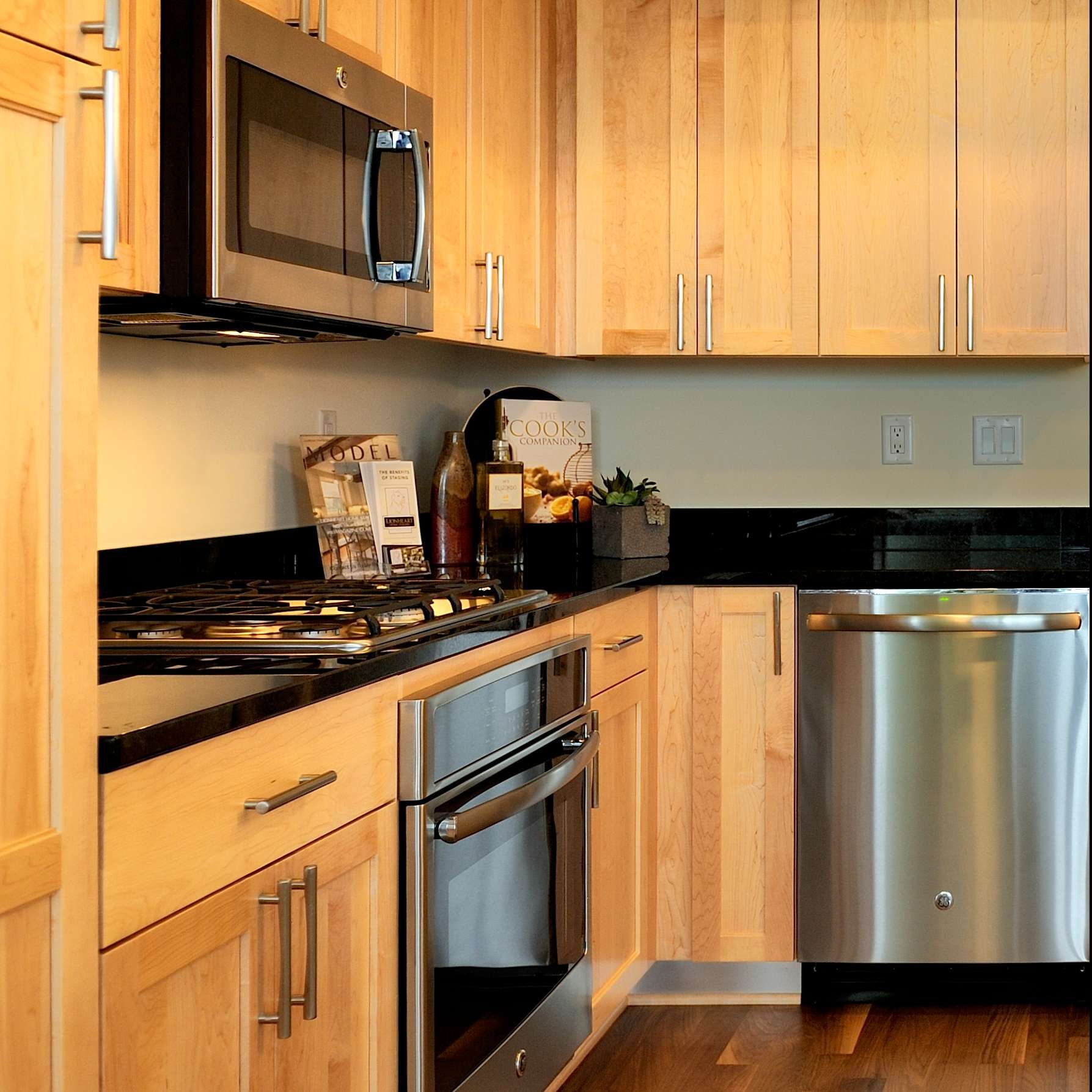 A modern kitchen with light wood cabinets, stainless steel appliances, and black countertops.