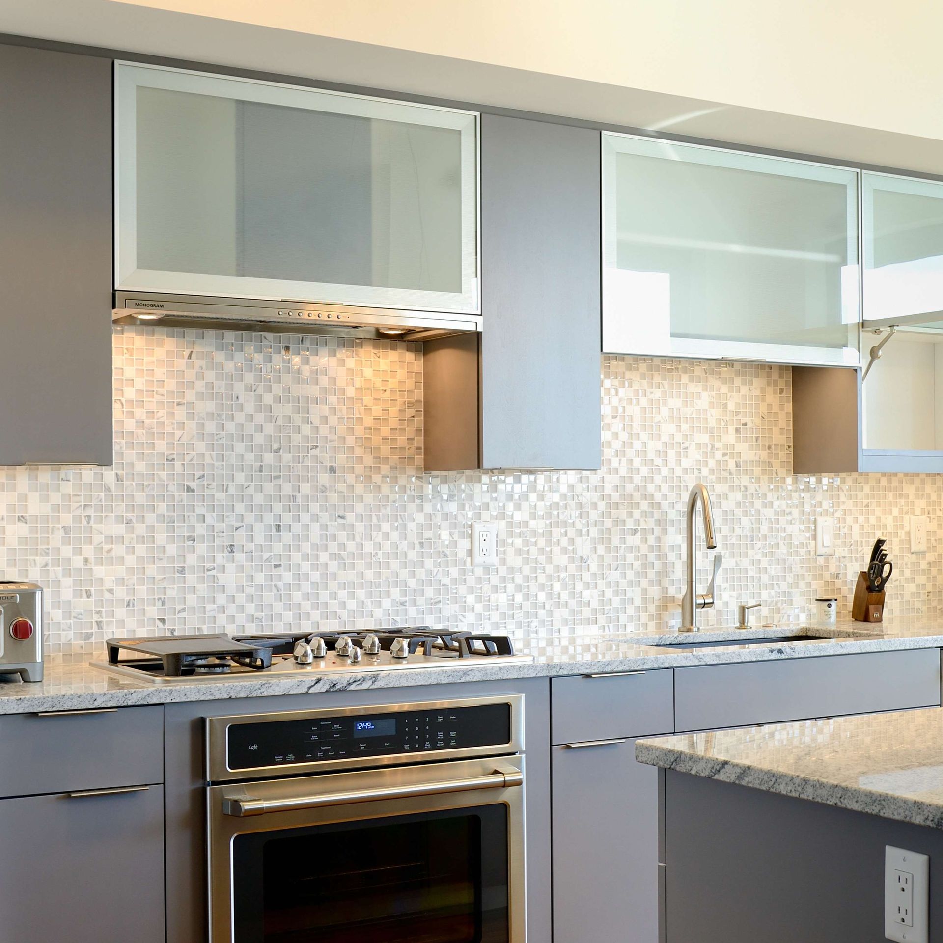 Modern kitchen with gray cabinets, a stainless steel oven, and a mosaic backsplash.