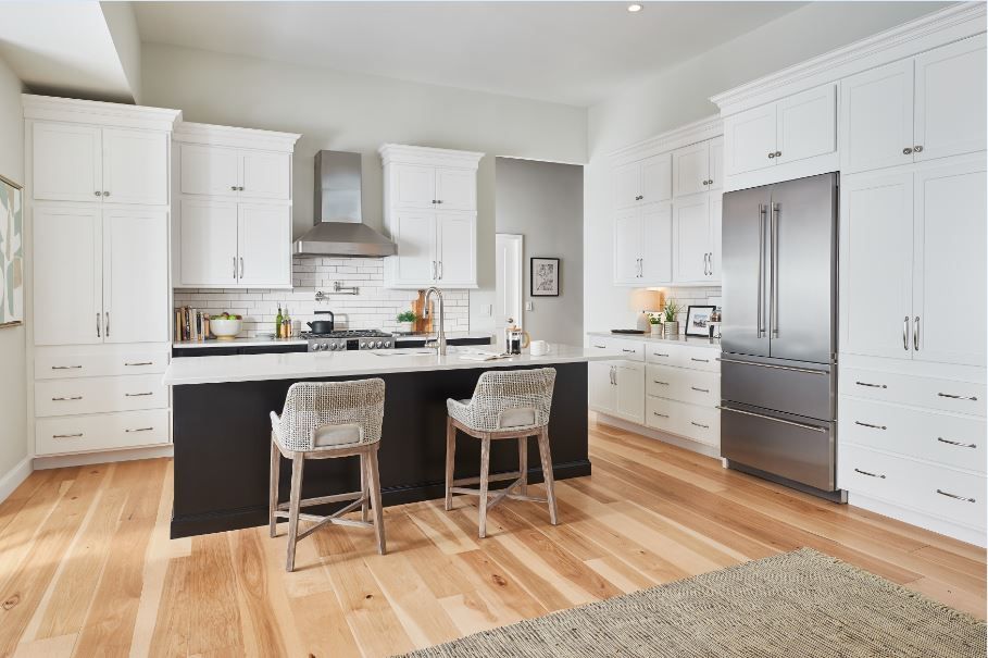 Modern white kitchen with black island, stainless steel appliances, and wood floors.