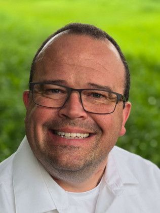 Man wearing glasses smiles outdoors with green background.