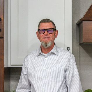 Man with glasses and goatee in a striped shirt, standing in front of white cabinets.