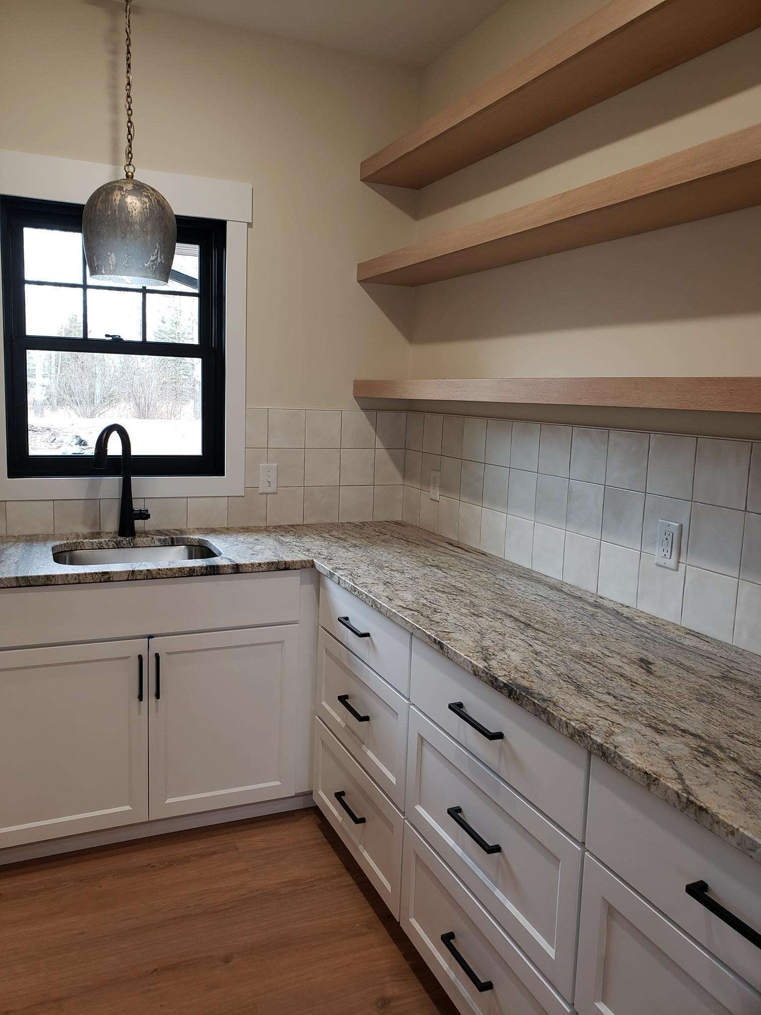 White kitchen with a black-framed window and cabinets. Floating shelves and granite countertop.