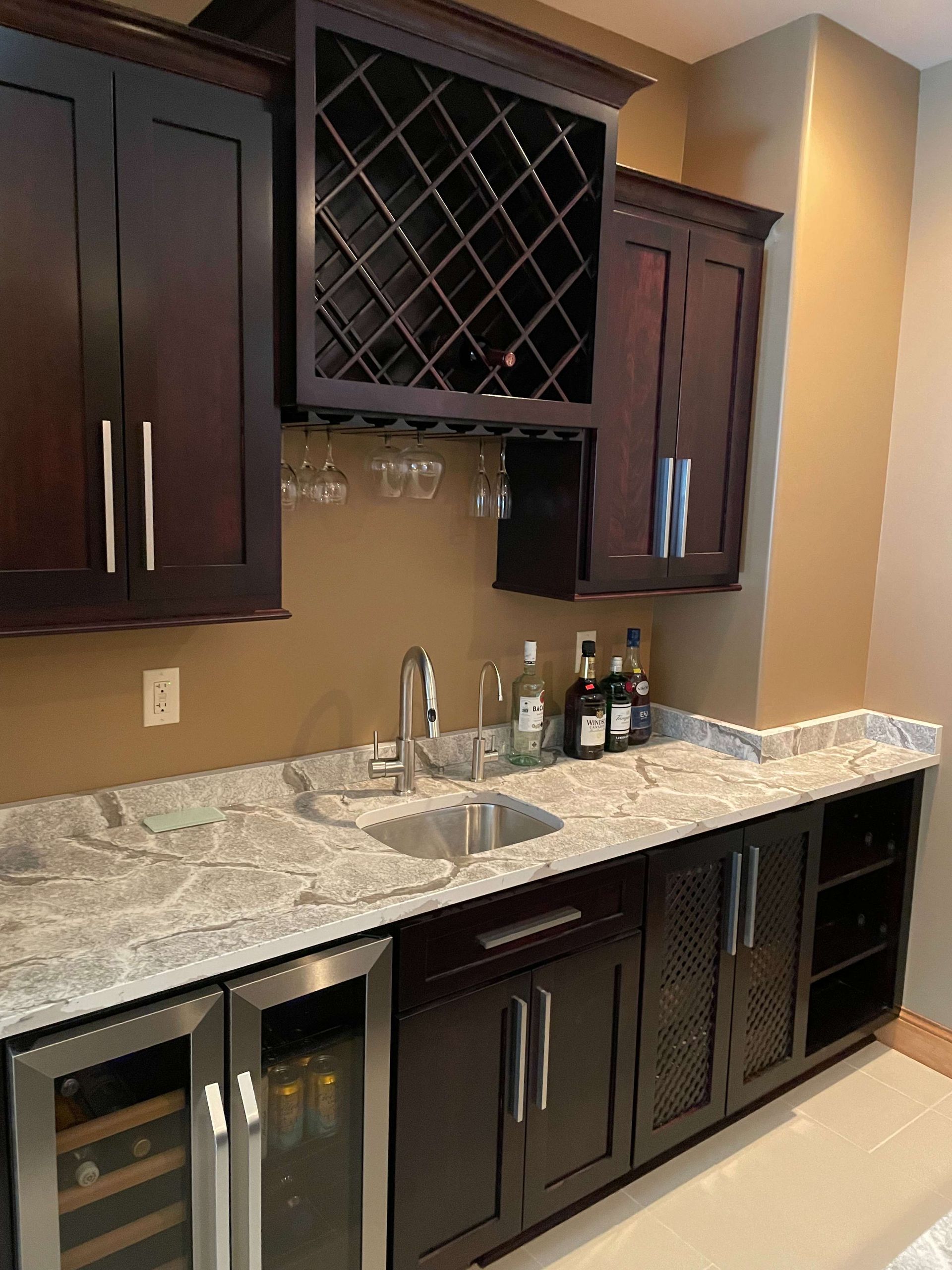 Dark wood home bar with granite countertop, sink, wine rack, and wine fridge.