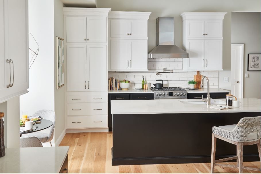 Kitchen with white cabinets, dark island, stainless steel appliances, and wood flooring.
