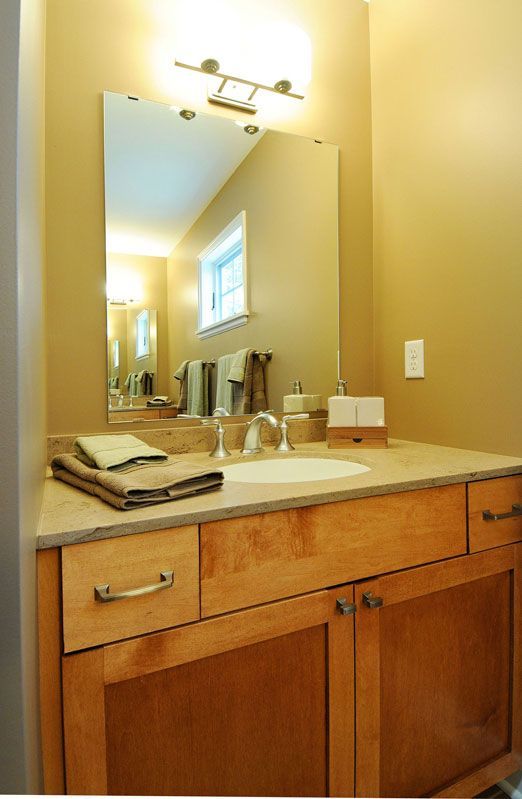 Bathroom with wooden vanity, rectangular mirror, and light fixture. Tan walls.