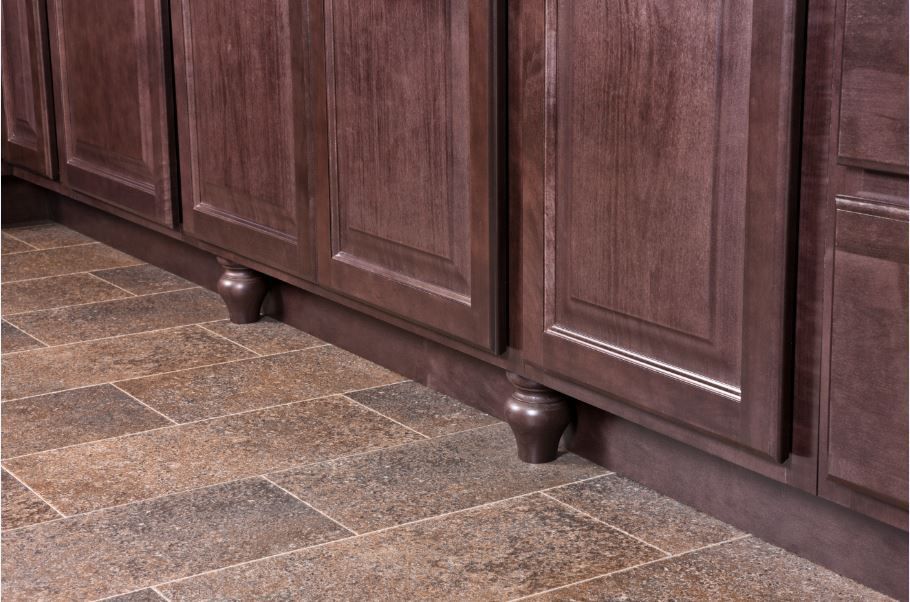 Brown kitchen cabinets with decorative feet against a tiled floor.