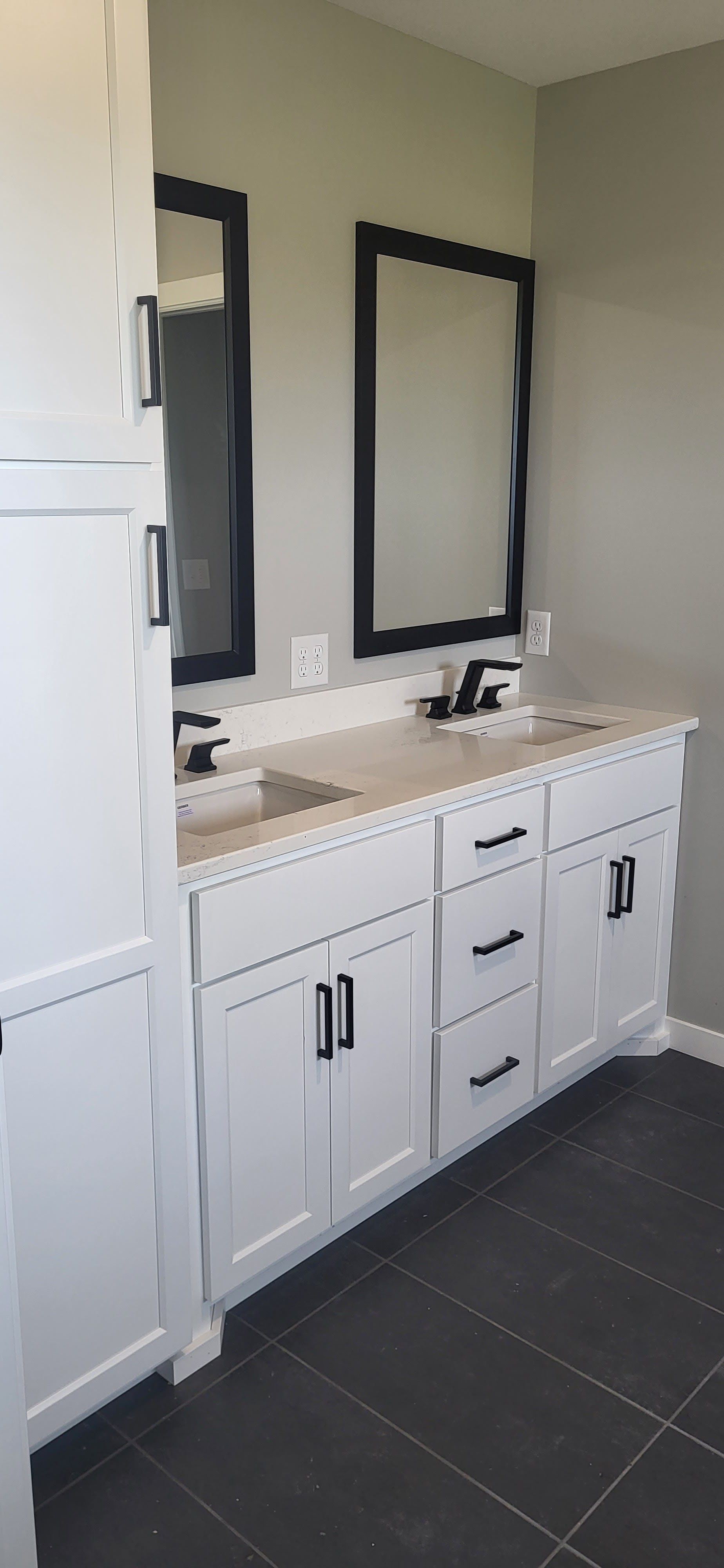 Bathroom with white cabinets, dark hardware and mirrors, and dark tiled floor.