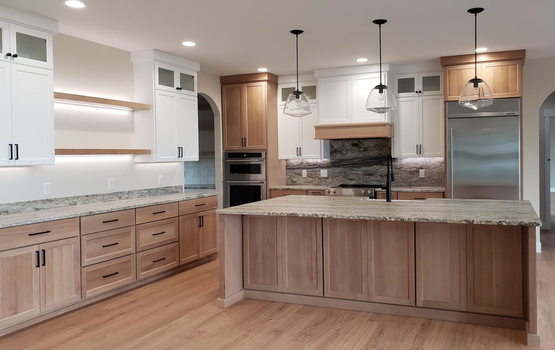 A modern kitchen with light wood cabinets, granite countertops, and a large island.
