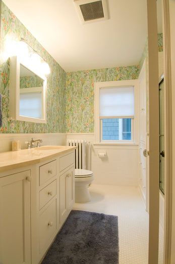 Bathroom with floral wallpaper, white vanity, and blue rug.