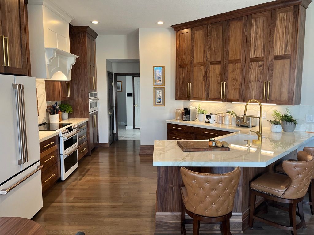 Kitchen with wood cabinets, white appliances, and a marble countertop. Two leather barstools.