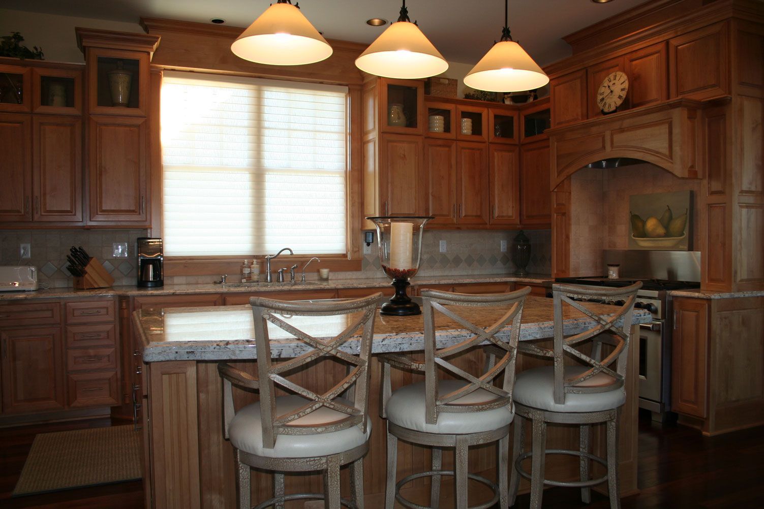 Kitchen with wooden cabinets, island with stools, three pendant lights, and a window.