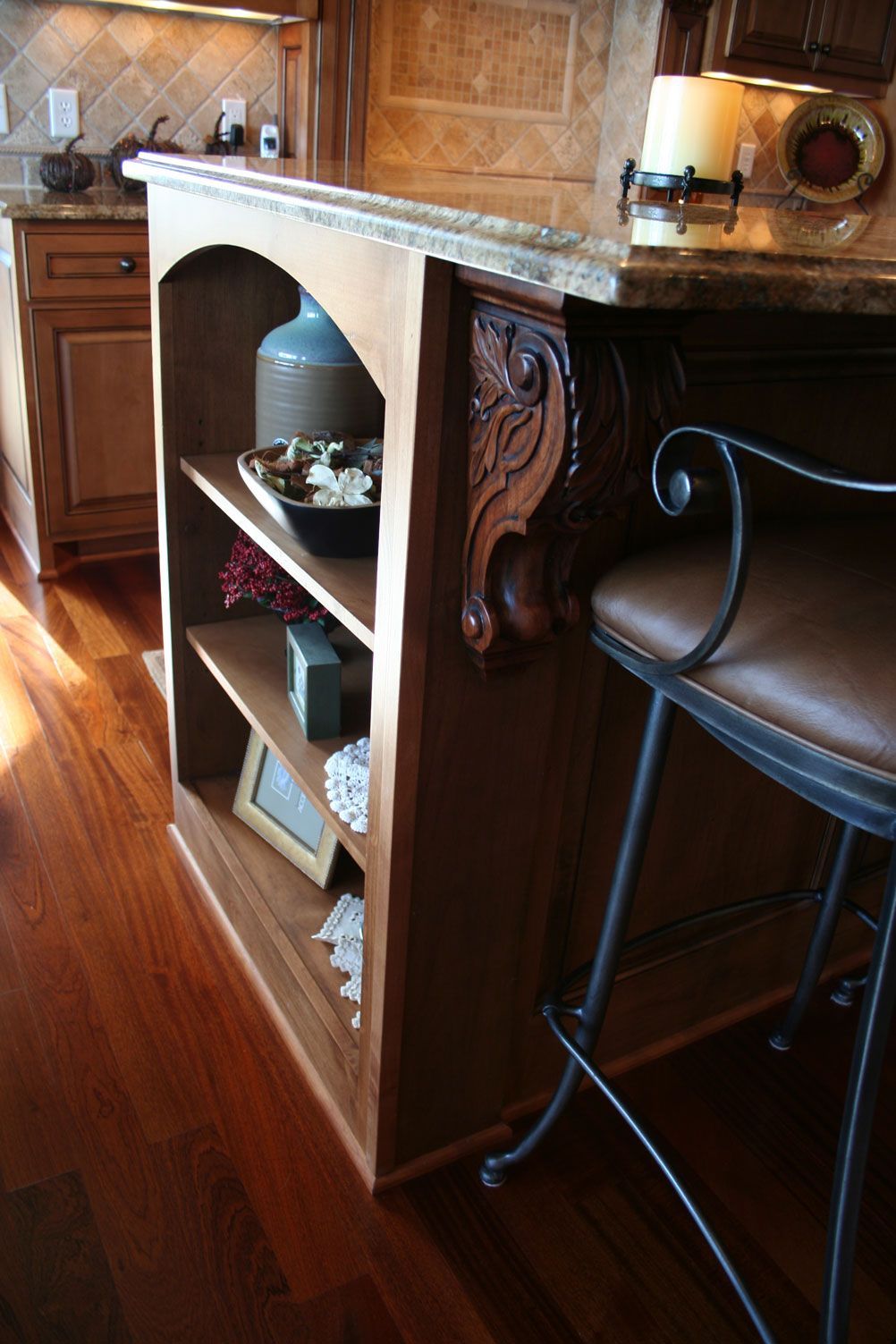 Wooden kitchen island with open shelving and ornate corbel, brown countertop, and dark wood flooring.