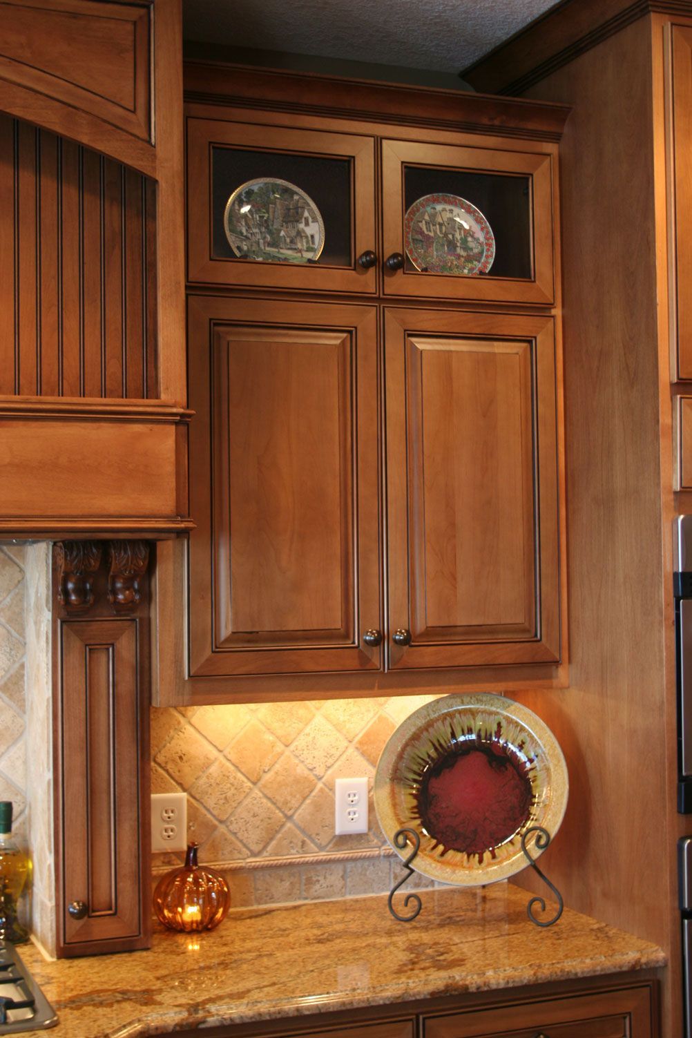Wooden kitchen cabinets with granite countertop, illuminated by under-cabinet lights. Decorative plates on display.
