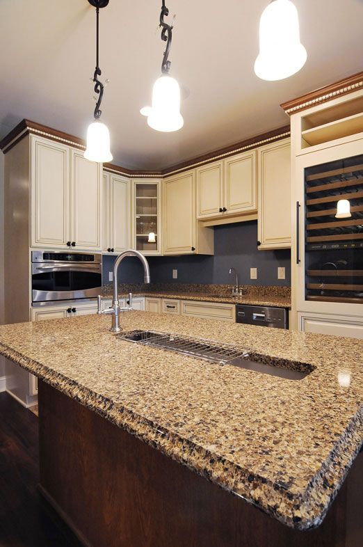 Kitchen with cream-colored cabinets, granite countertops, and island with sink. Three pendant lights hang above.